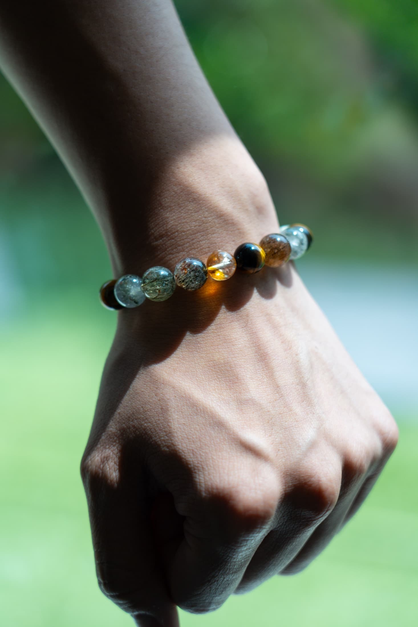 A MoonArq bracelet of phantom quartz, beryl, tiger's eye and golden rutilated quartz, worn on the wrist in sunlight